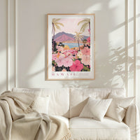 a framed poster of a tropical landscape with palm trees, flowers, and mountains, hanging on a wall above a white couch with a blanket draped over it.