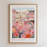 The image is a framed poster depicting a vibrant and colorful scene from the Flower Market in Beaufort, featuring a variety of flowers and buildings in shades of pink, orange, and yellow.