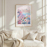 a framed poster of a cityscape with a floral design, hanging on a wall above a white couch with a blanket draped over it.