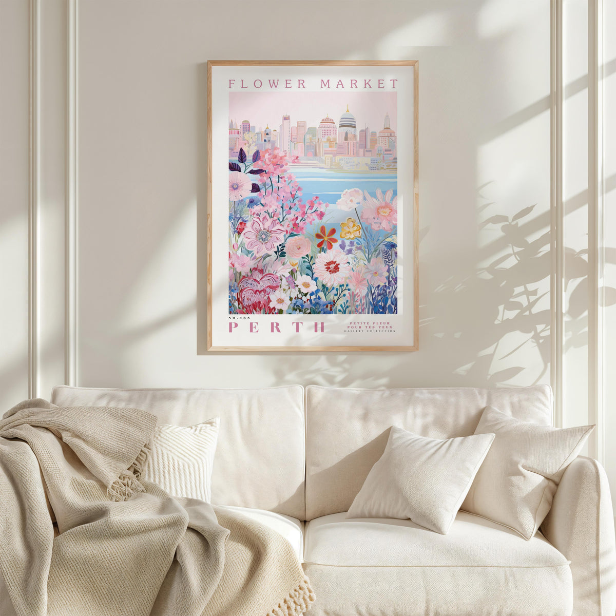 a framed poster of a cityscape with a floral design, hanging on a wall above a white couch with a blanket draped over it.
