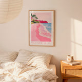 a bedroom scene with a framed poster of a beach on the wall, a bed with striped pillows, and a nightstand with a coffee mug and books.
