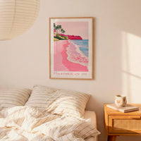 a bedroom scene with a framed poster of a beach on the wall, a bed with striped pillows, and a nightstand with a coffee mug and books.