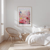 a bedroom with a bed, a woven chair, and a framed poster of a flower market in Dallas hanging on the wall.