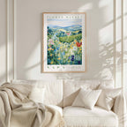 a framed poster of a field of flowers hanging on a wall above a white couch with a blanket draped over it.