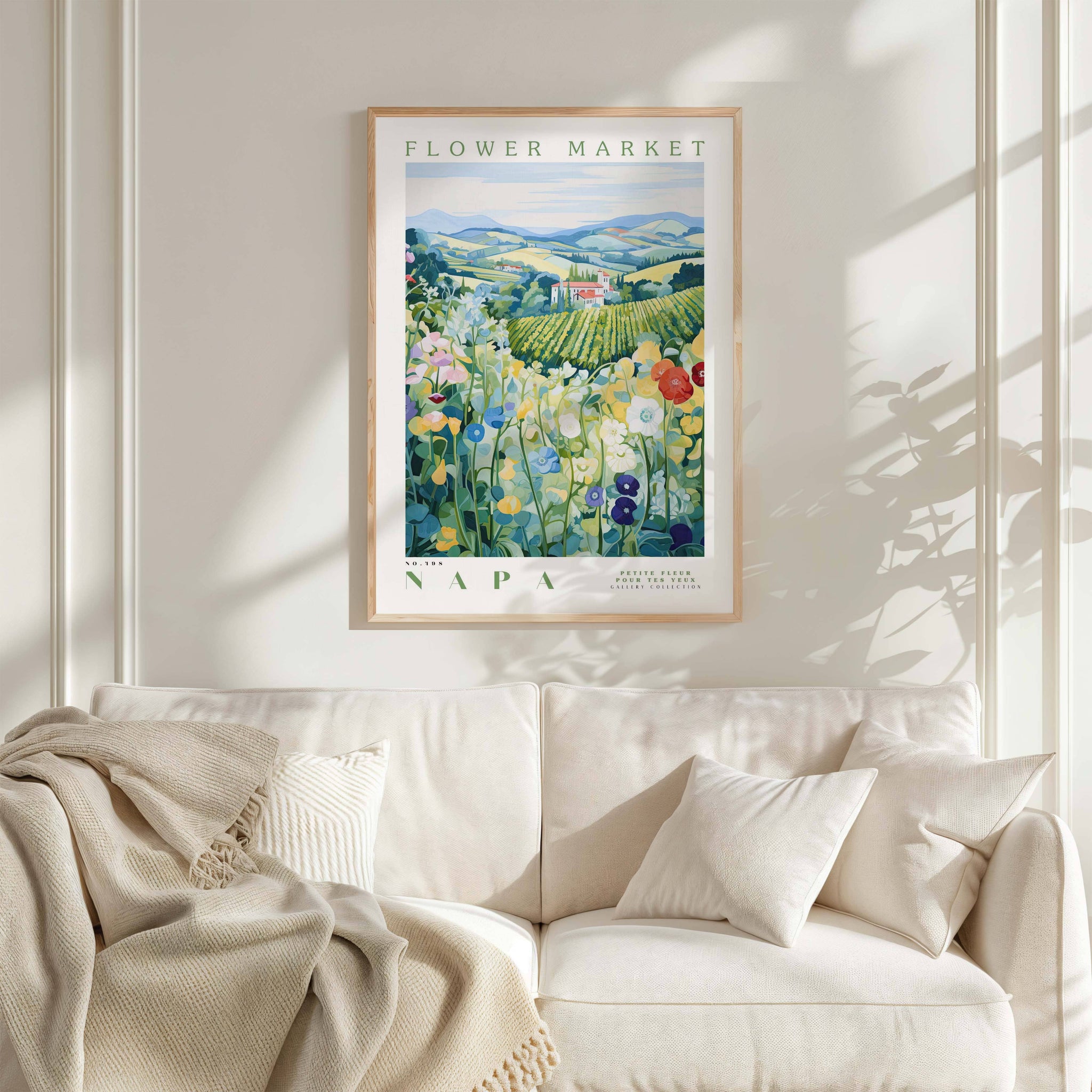 a framed poster of a field of flowers hanging on a wall above a white couch with a blanket draped over it.