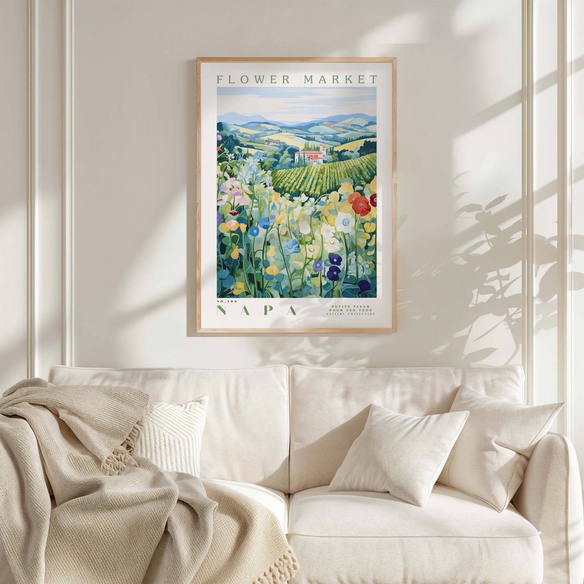 a framed poster of a field of flowers hanging on a wall above a white couch with a blanket draped over it.