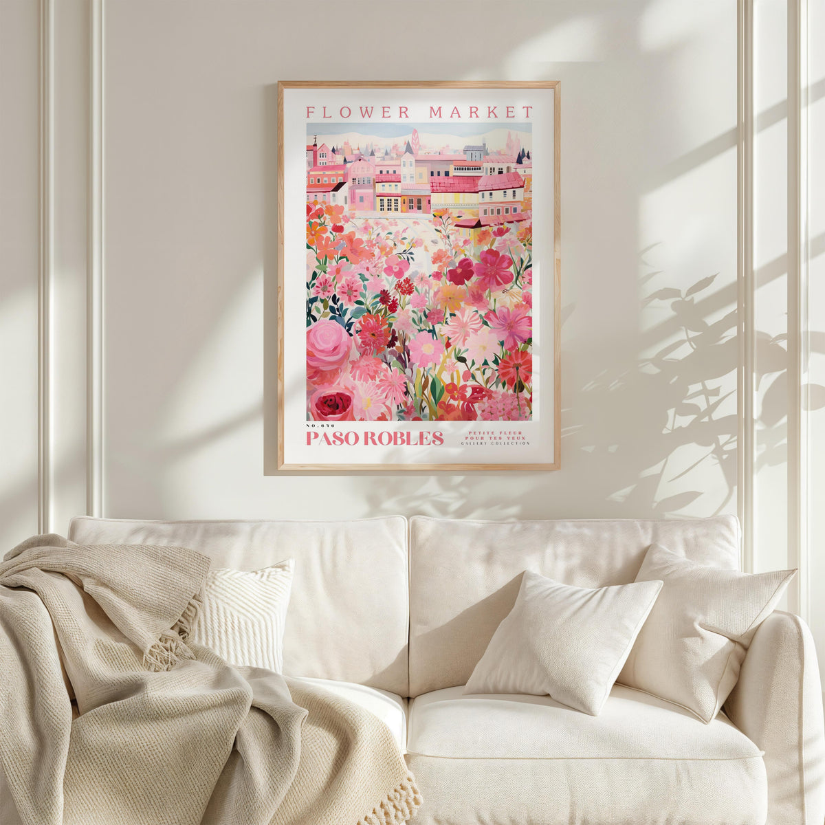 a framed poster of a colorful floral scene hanging on a wall above a white couch with a blanket draped over it.