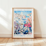 A framed poster of a colorful floral scene, with the text "FLOWER MARKET Santorini" and "Petite Florier Galerie Collection" printed on it.
