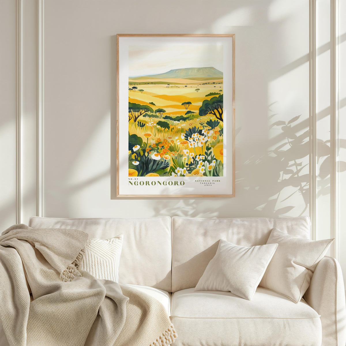 a framed poster of a field with flowers hanging on a wall above a white couch with pillows.