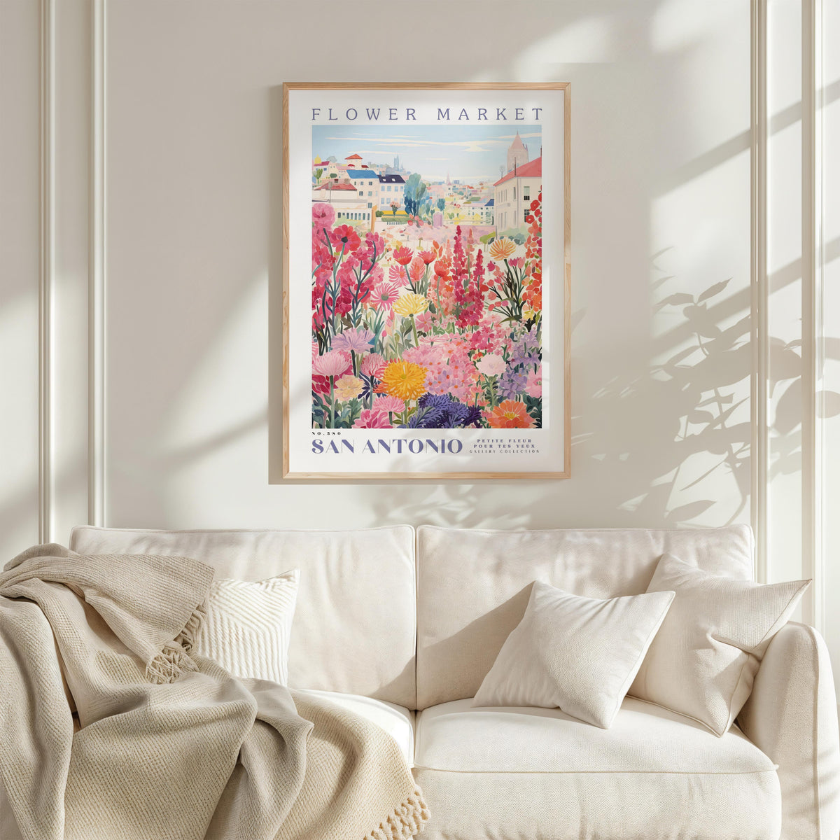 a framed poster of a colorful garden scene hanging on a wall above a white couch with a blanket draped over it.