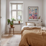 a cozy bedroom with a large bed, a nightstand with a potted plant, and a framed poster of a cityscape on the wall.