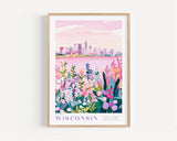 A framed poster depicting a cityscape with a pink sky and a field of colorful flowers in the foreground.