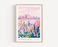 A framed poster depicting a cityscape with a pink sky and a field of colorful flowers in the foreground.