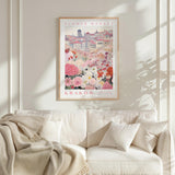 a framed poster of a flower market in Krakow, Poland, hanging on a white wall above a white couch with a blanket draped over it.