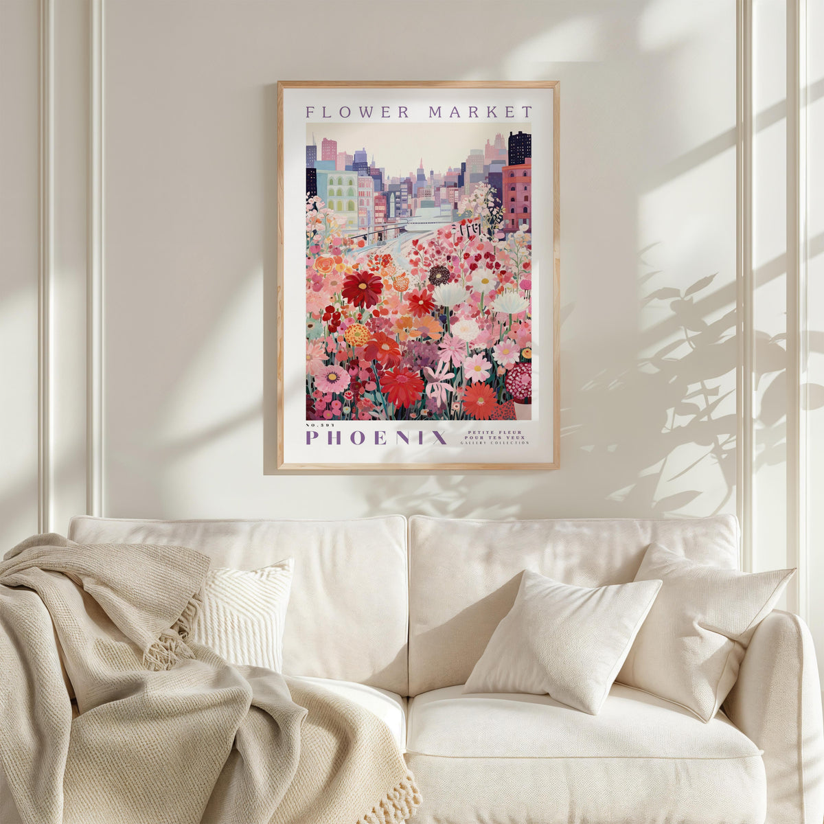 a framed poster of a cityscape with a flower market in the background, hanging on a wall above a white couch with a blanket draped over it.