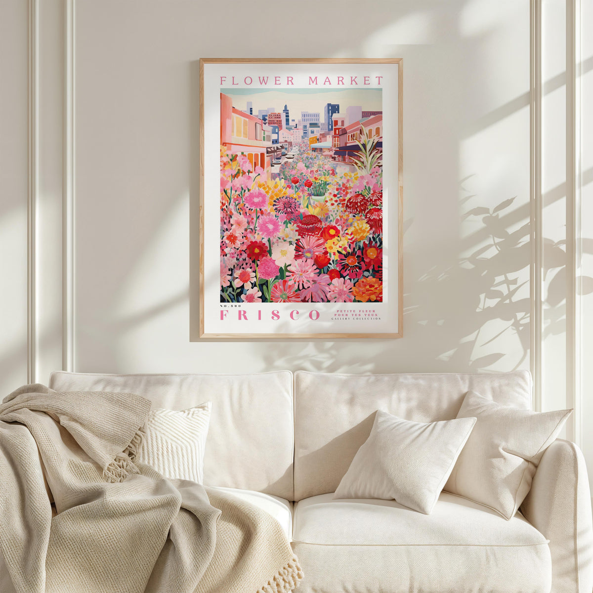a framed poster of a vibrant flower market in Frisco, California, hanging on a white wall above a white couch with a blanket draped over it.