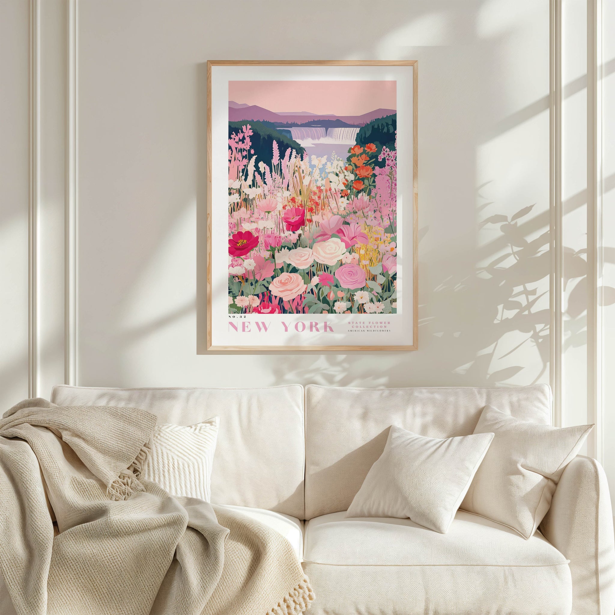 a framed poster of a colorful floral scene hanging on a wall above a white couch with a blanket draped over it.
