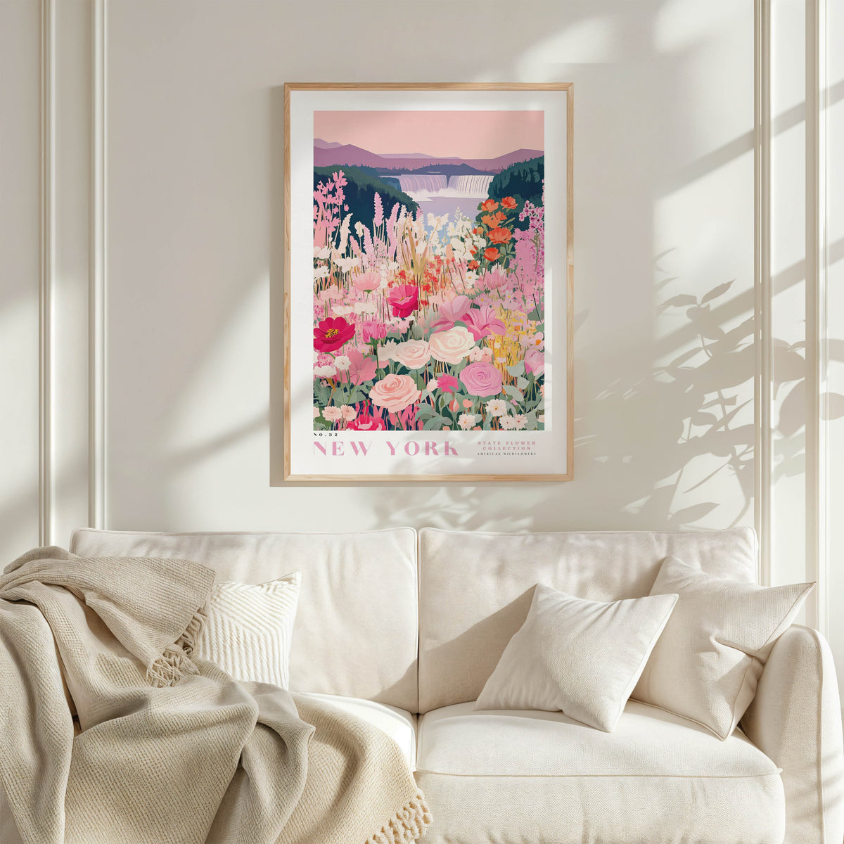 a framed poster of a colorful floral scene hanging on a wall above a white couch with a blanket draped over it.