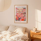 a bedroom scene with a framed poster of a flower market hanging on the wall above a bed with striped pillows.