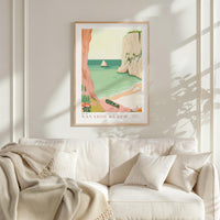 a framed poster of a beach scene with a boat, hanging on a wall above a white couch with a blanket draped over it.