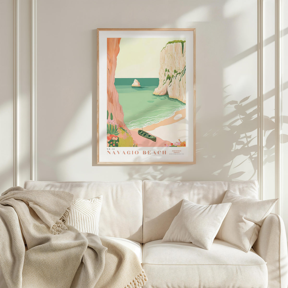 a framed poster of a beach scene with a boat, hanging on a wall above a white couch with a blanket draped over it.