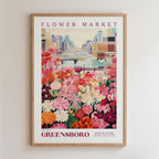 A framed poster depicting a vibrant flower market in Greensboro, North Carolina. The poster features a colorful illustration of a flower market with various types of flowers and plants, set against a backdrop of a cityscape.