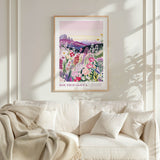 a framed poster of a colorful floral landscape hanging on a wall above a white couch with a blanket draped over it.
