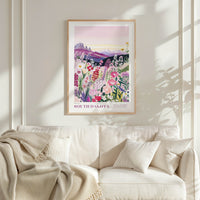 a framed poster of a colorful floral landscape hanging on a wall above a white couch with a blanket draped over it.