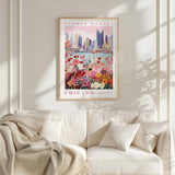 a poster of a cityscape with a flower market in the foreground, hanging on a wall above a white couch.