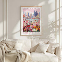 a poster of a cityscape with a flower market in the foreground, hanging on a wall above a white couch.