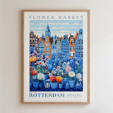The image is a framed poster depicting a vibrant flower market in Rotterdam, Netherlands. The poster showcases a variety of colorful flowers and plants arranged in vases, set against the backdrop of the city's distinctive architecture. The text on the poster reads "FLOWER MARKET" and "NEW YORK ROTTERDAM POTÉ TÉ FEU, GALLERY COLLECTION".