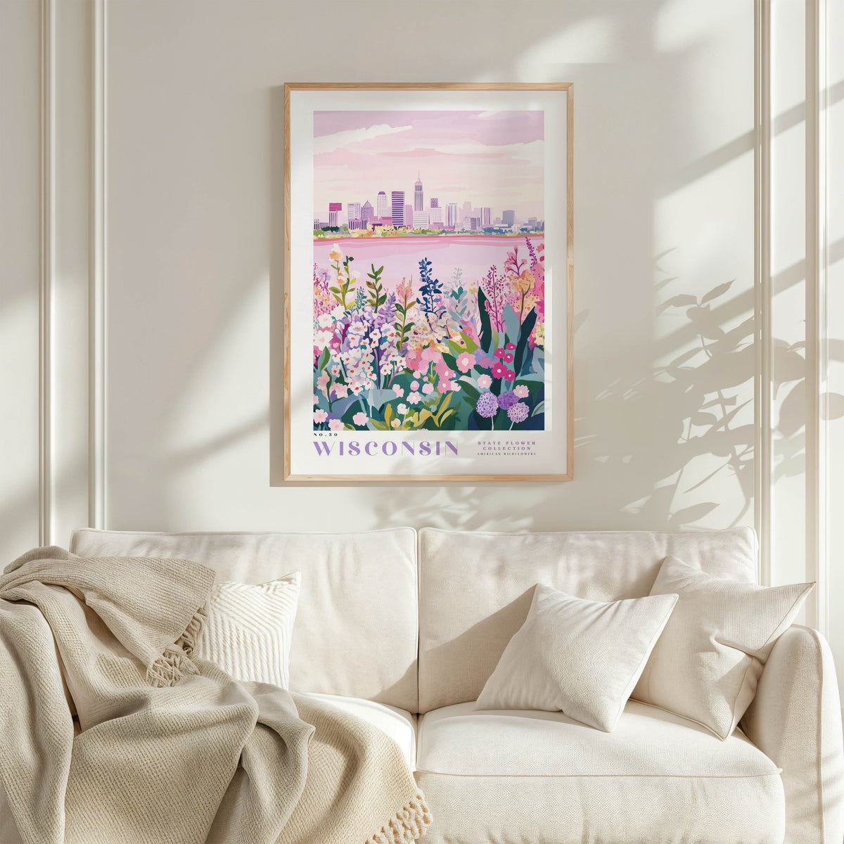 a framed poster of a cityscape with a floral background, hanging on a wall above a white couch with a blanket draped over it.