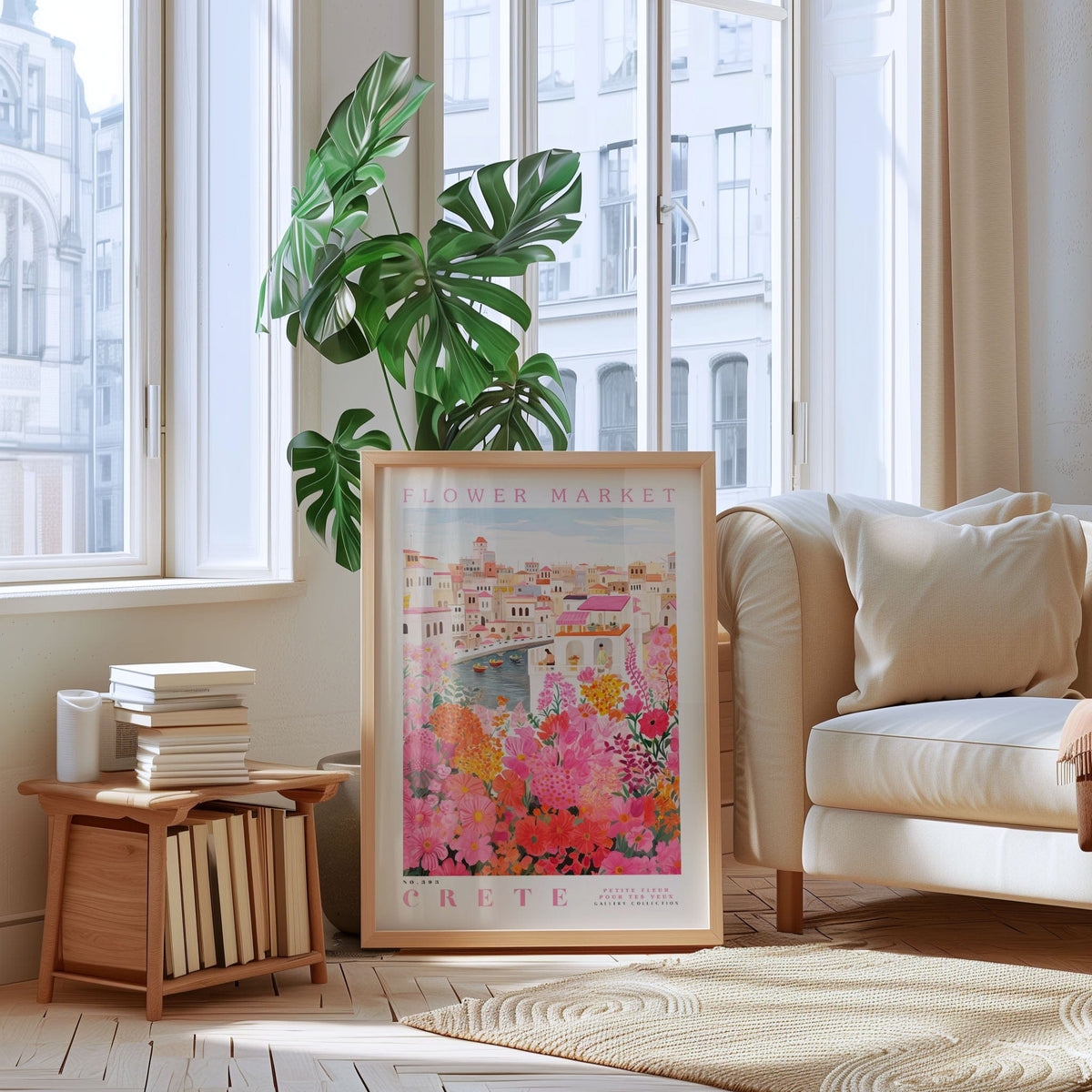 a living room with a large framed poster of a colorful floral scene hanging on the wall, a stack of books on a wooden shelf, a white sofa, and a large window with a view of a city.