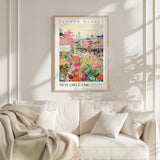 a framed poster of a colorful and vibrant scene from the Flower Market in New Orleans, with a white couch and a blanket in the foreground.