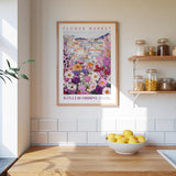 a kitchen scene with a framed poster of a colorful flower market on the wall, a wooden counter with a bowl of lemons, and shelves displaying various jars and containers.