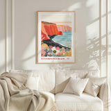 a framed poster of a scenic coastal landscape with a cliff overlooking the ocean, hanging on a wall above a white couch with pillows.