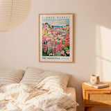 a bedroom scene with a framed poster of a flower market hanging on the wall above a bed with striped pillows.