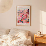 a bedroom scene with a framed poster of a colorful floral market hanging on the wall above a bed with striped pillows.