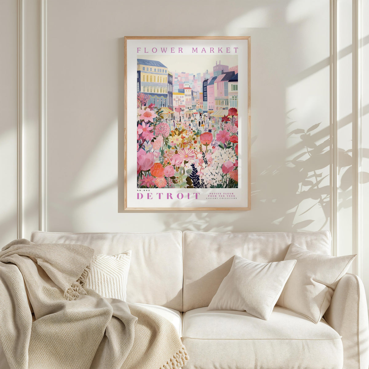 a framed poster of a colorful cityscape with flowers, hanging on a wall above a white couch with pillows.