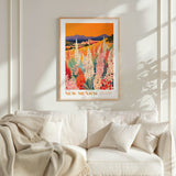 a framed poster of a colorful field of flowers hanging on a wall above a white couch with a blanket draped over it.