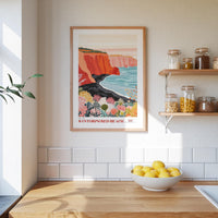 a kitchen counter with a bowl of lemons, a framed poster of Santornir Beach, and shelves with jars and bottles.
