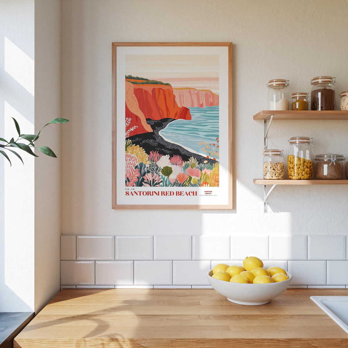a kitchen counter with a bowl of lemons, a framed poster of Santornir Beach, and shelves with jars and bottles.