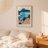 a bedroom scene with a framed poster of a tropical beach landscape hanging on the wall above a bed with striped pillows.