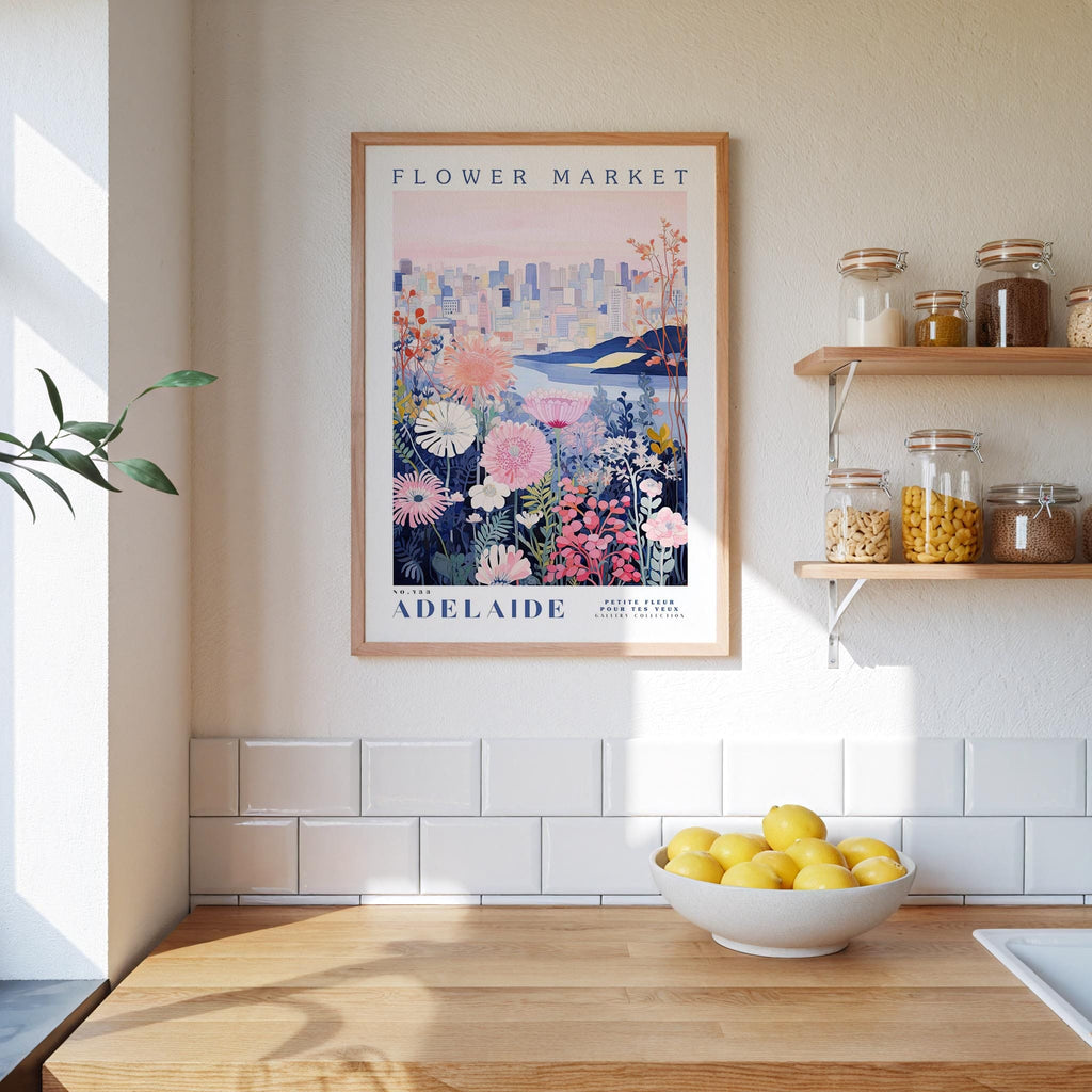 a framed poster of a flower market in Adelaide, Australia, hanging on a wall above a kitchen counter with a bowl of lemons and jars of food on the counter.