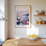 a framed poster of a flower market in Adelaide, Australia, hanging on a wall above a kitchen counter with a bowl of lemons and jars of food on the counter.