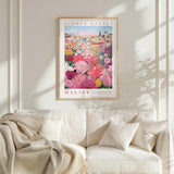 a framed poster of a colorful floral scene hanging on a wall above a white couch with a blanket draped over it.