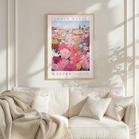 a framed poster of a colorful floral scene hanging on a wall above a white couch with a blanket draped over it.