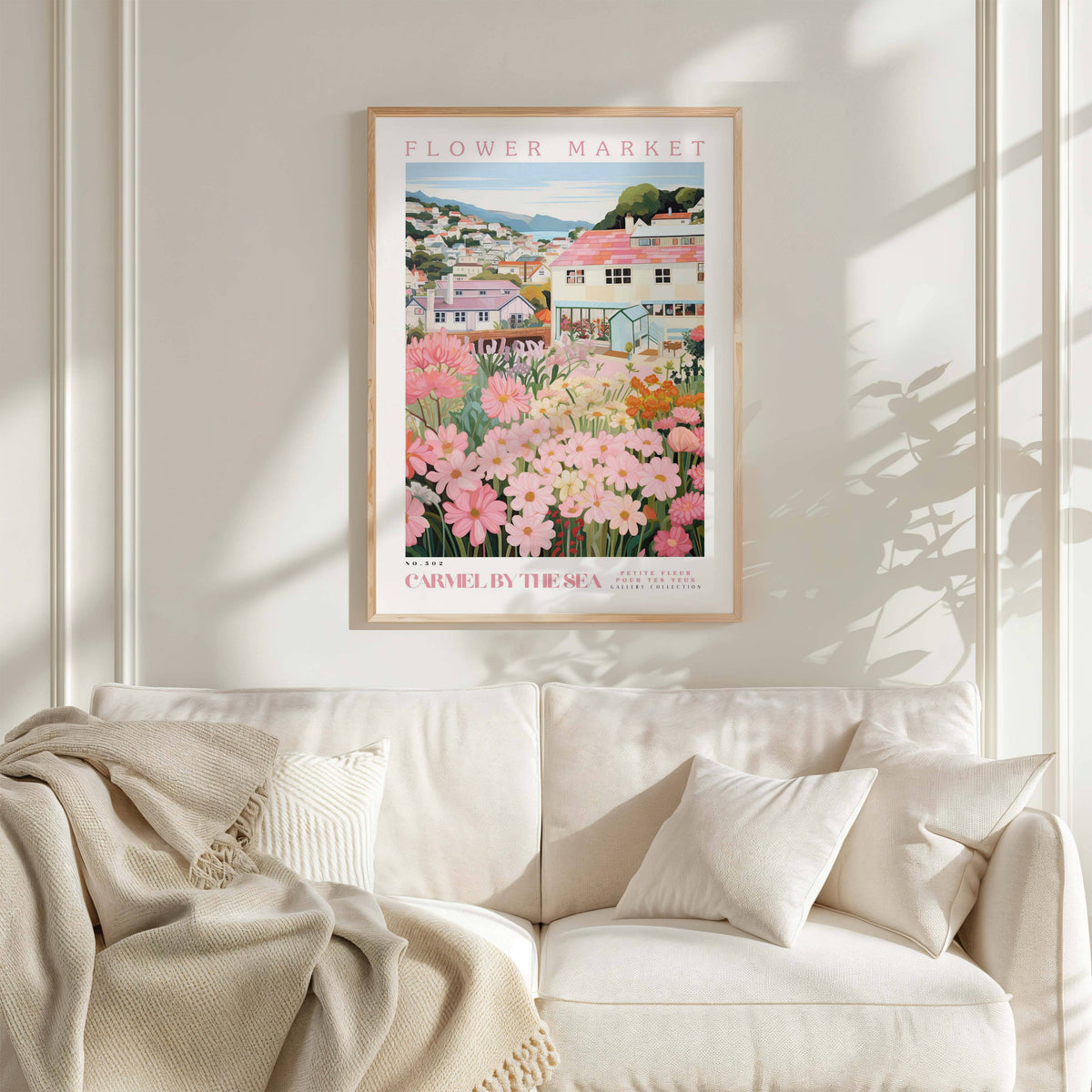 a framed poster of a flower market, with a white couch and a blanket in the foreground.