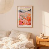 a bedroom scene with a framed poster of a flower market hanging on the wall above a bed with striped pillows.