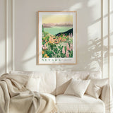 a framed poster of a scenic landscape with mountains and a lake, hanging on a wall above a white couch with a blanket draped over it.